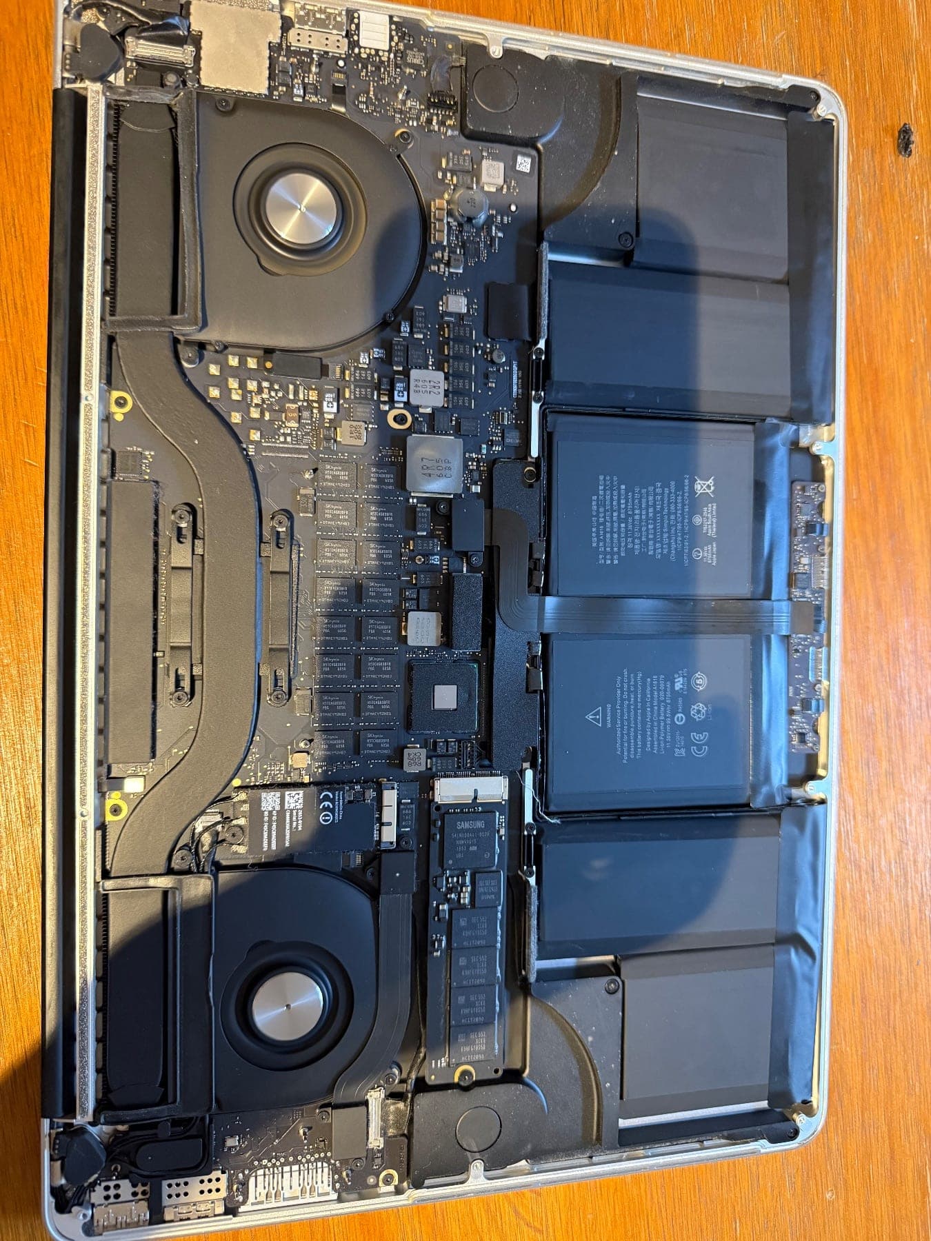 MacBook Pro 15-inch with the bottom case removed, showing the logic board, two fans and the battery cells in place