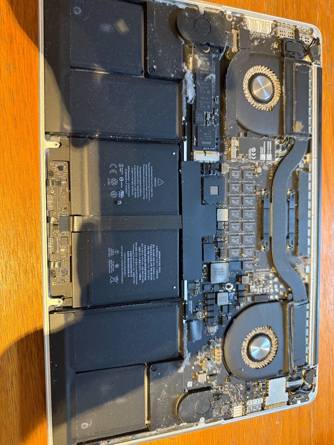 MacBook Pro internals with battery cells fitted, dust and lint visible on the fans and board