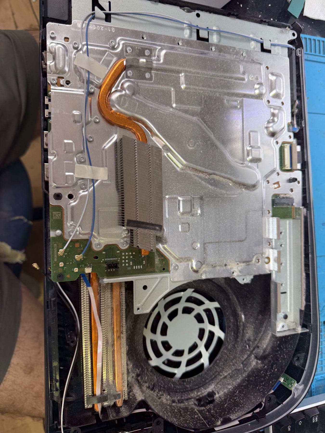 PS5 opened up on a bench showing the metal shielding, copper heat pipe and fan, all coated in grey dust
