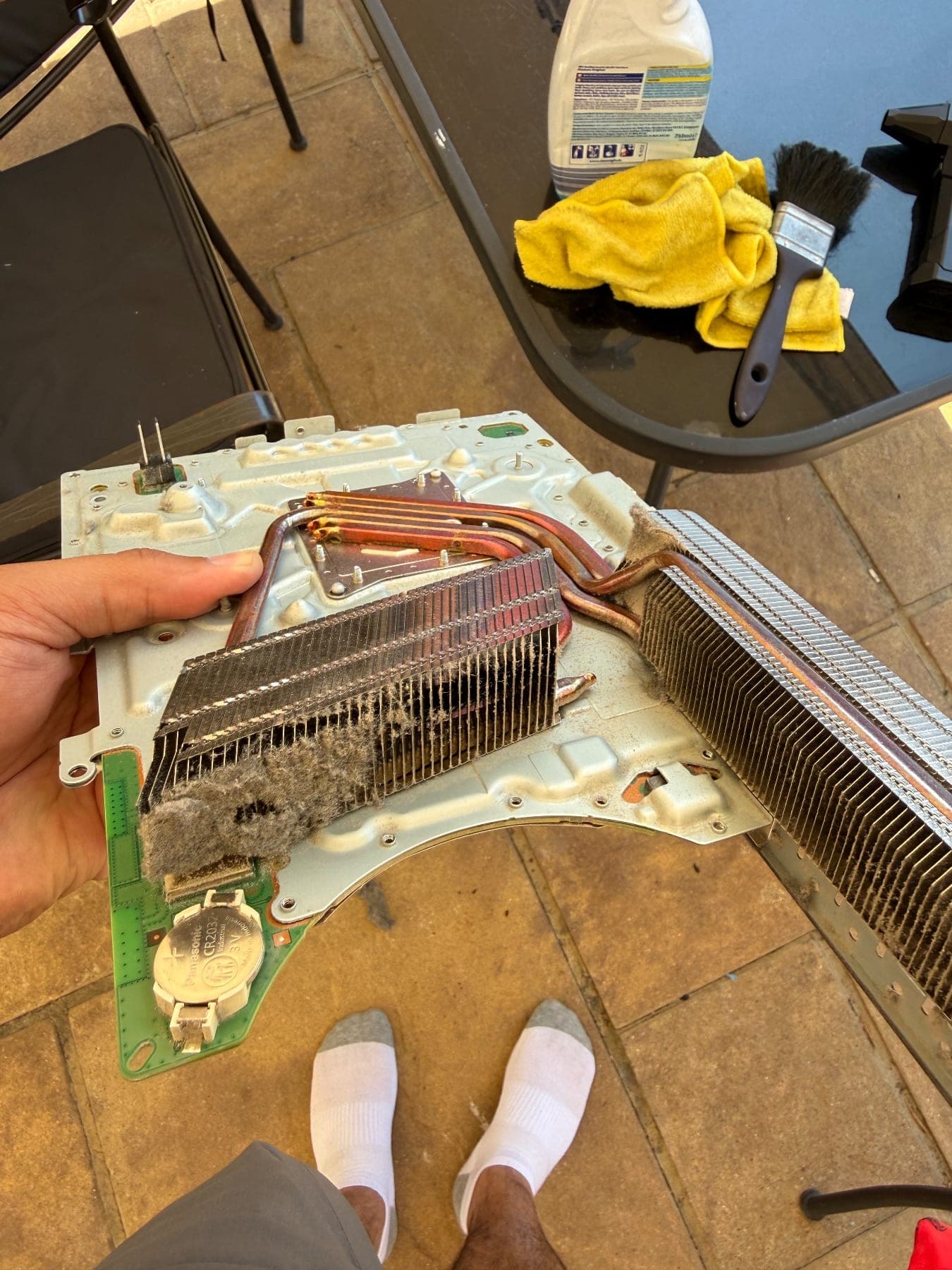 Heatsink assembly held in one hand, with thick felted dust matted between the fins and the copper heat pipes visible